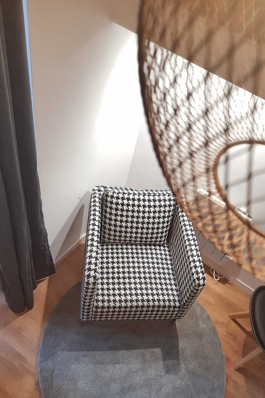 Fauteuil design en tissu motif pied-de-poule noir et blanc dans un salon moderne avec parquet et tapis rond gris