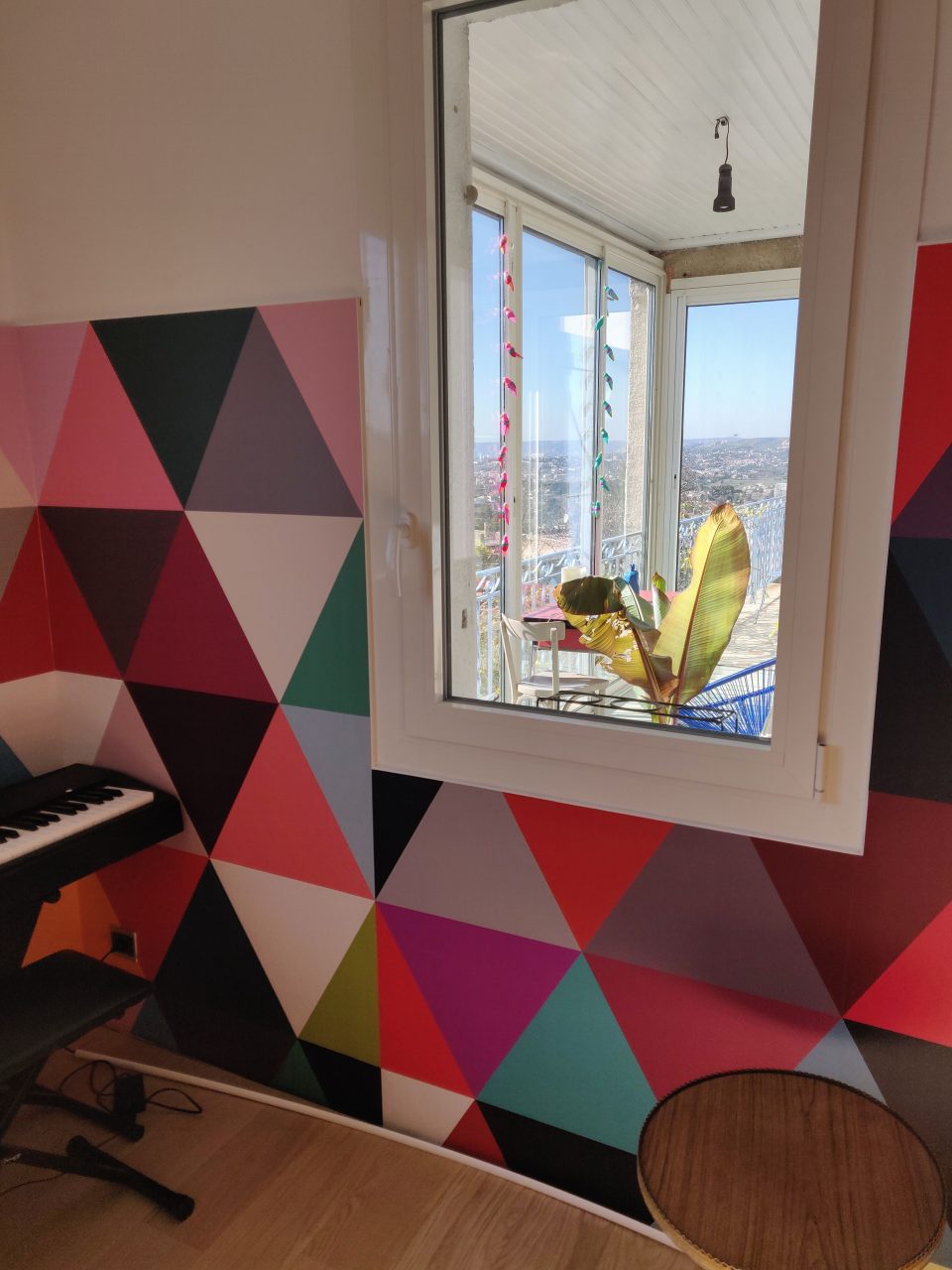 Tapisserie triangulaire colorée encadrant une fenêtre, formes graphiques intérieur salon