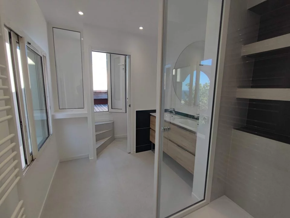 Baño reformado al completo: ducha con vistas al mar, pavimento de piedra, doble lavabo y acceso a la terraza solarium