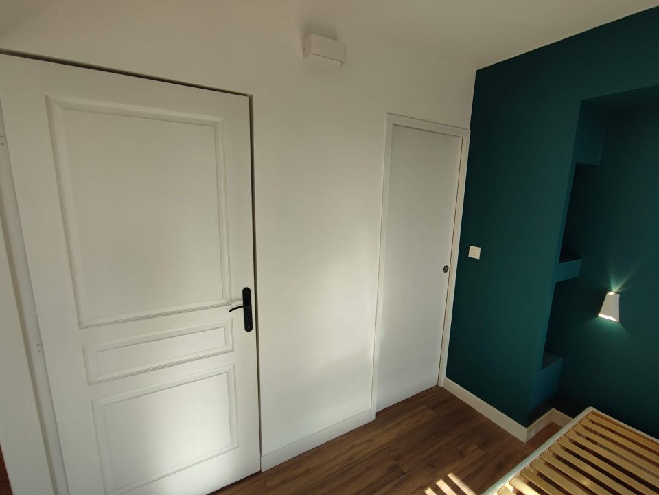 Suite parentale de 19,75 m² réalisée : chambre avec tête de lit intégrée, niches électrifiées et accès à la loggia réintégrée