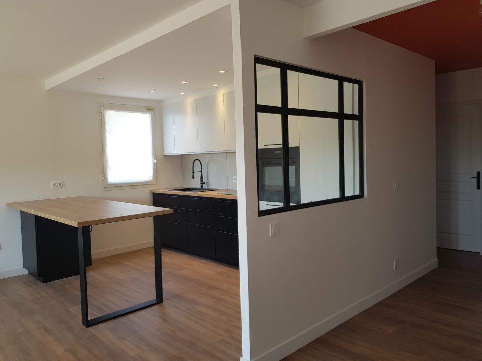 Cuisine ouverte réalisée avec verrière noire vers l’entrée et table îlot dans un appartement T4 de 93 m²